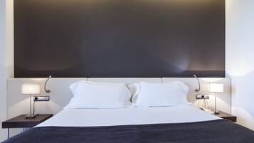 A neatly made bed with white linens and a dark throw blanket, flanked by two bedside tables with lamps.