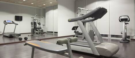 Un gimnasio con equipo de ejercicio, incluyendo cintas de correr, un banco y pesas.