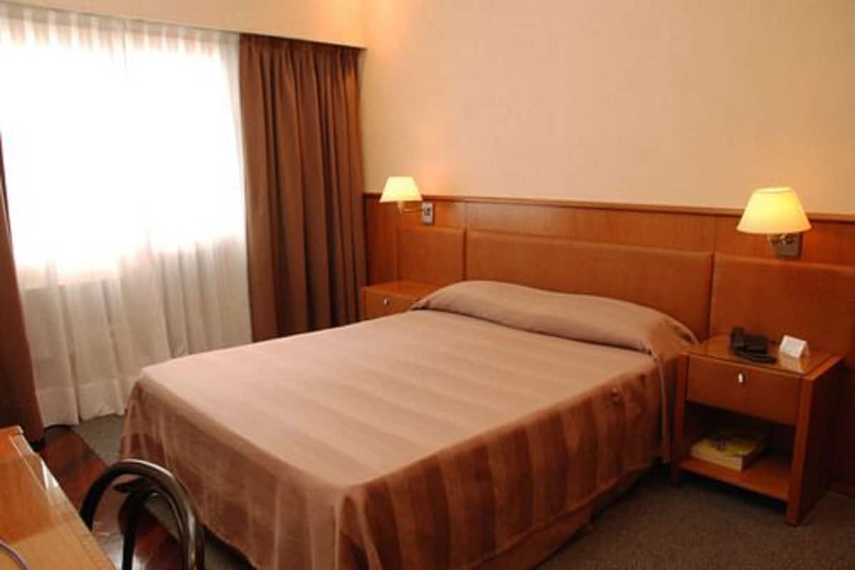 Una habitación de hotel con una cama individual, dos lámparas de noche, una mesita de noche y una silla.
