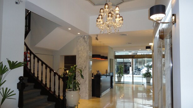 A modern lobby with a marble floor, a grand chandelier, a staircase with dark wooden railings, and potted plants. - Hotel Napoleon (Buenos Aires)