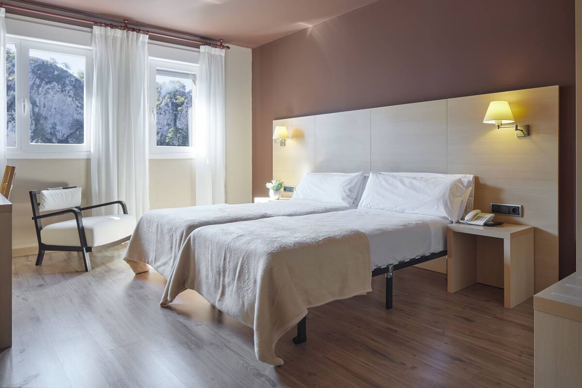 A hotel room with two beds, a desk, a chair, and a window with curtains.