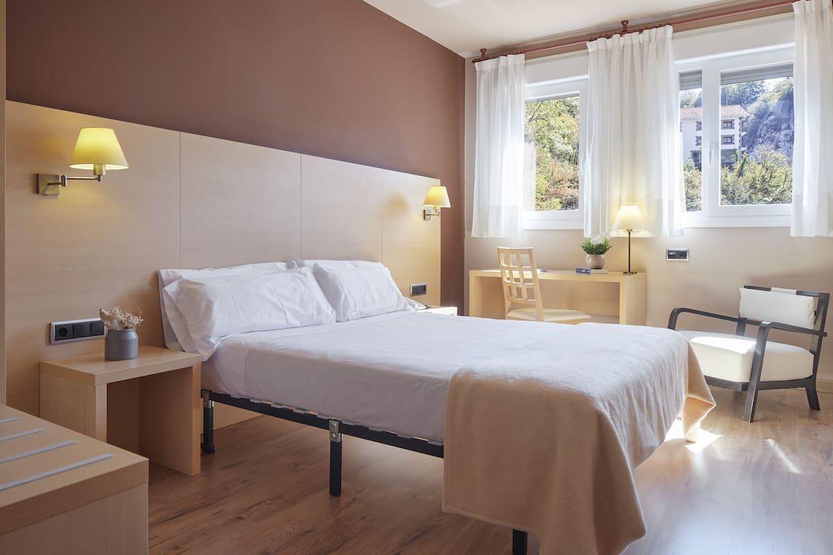 A hotel room with a bed, bedside tables, a desk, a chair, and a window with curtains.