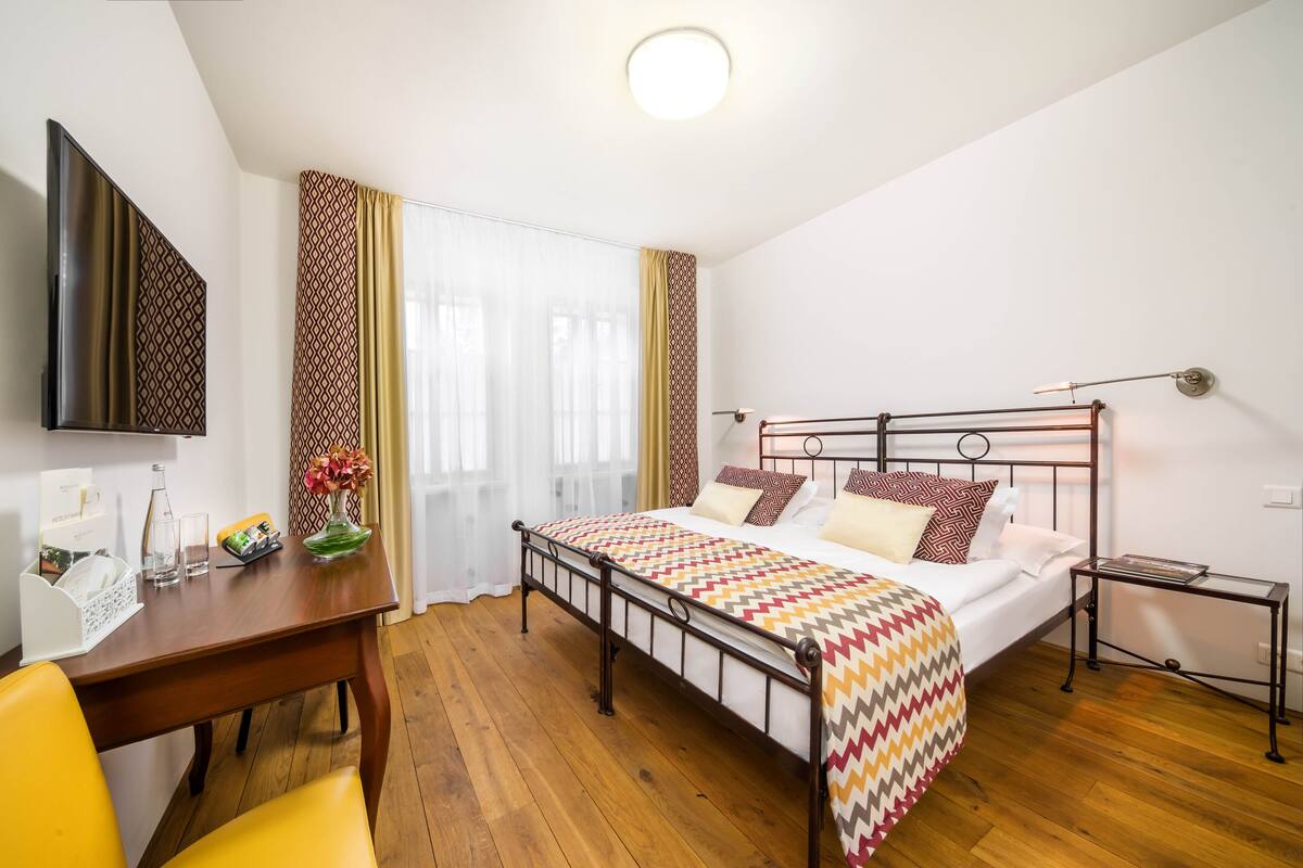 Una habitación de hotel moderna con cama, mesita de noche, lámpara, televisor y un escritorio con silla.