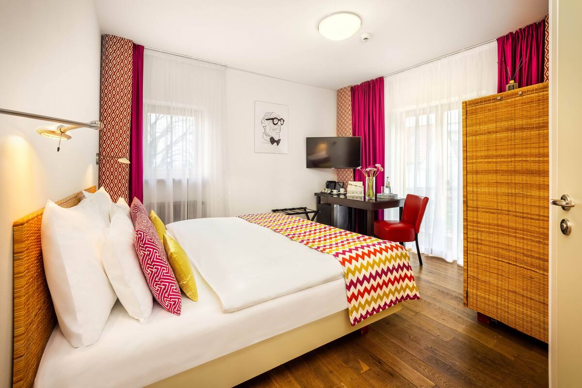 Una habitación de hotel con cama, escritorio, silla, televisor y armario.