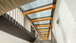 Una escalera moderna con paneles de vidrio y vigas de madera, que conduce a un piso superior.