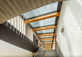 Una escalera moderna con paneles de vidrio y vigas de madera, que conduce a un piso superior.