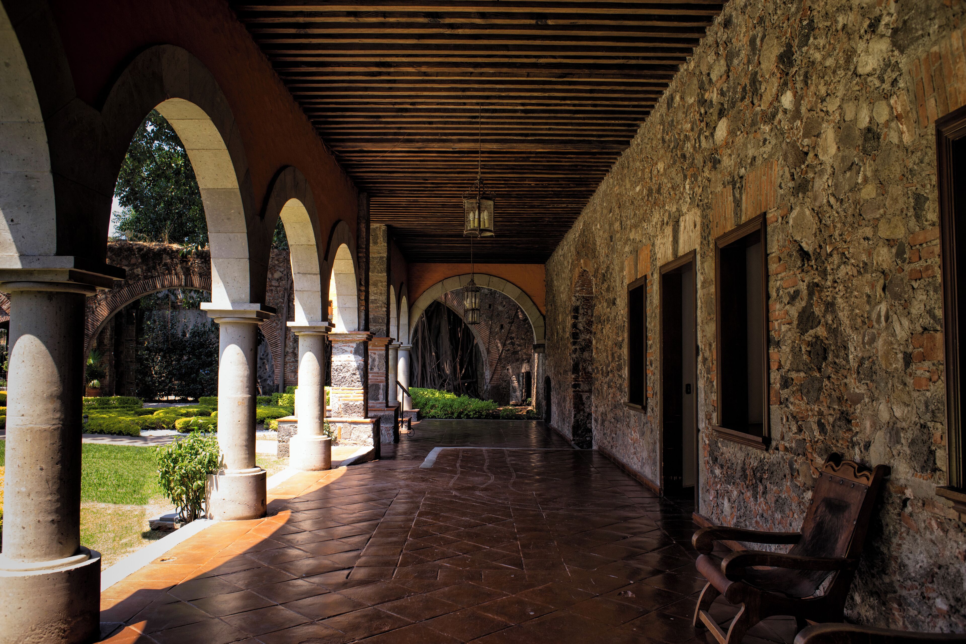 Un patio interior con columnas de piedra, arcos y techo de madera.