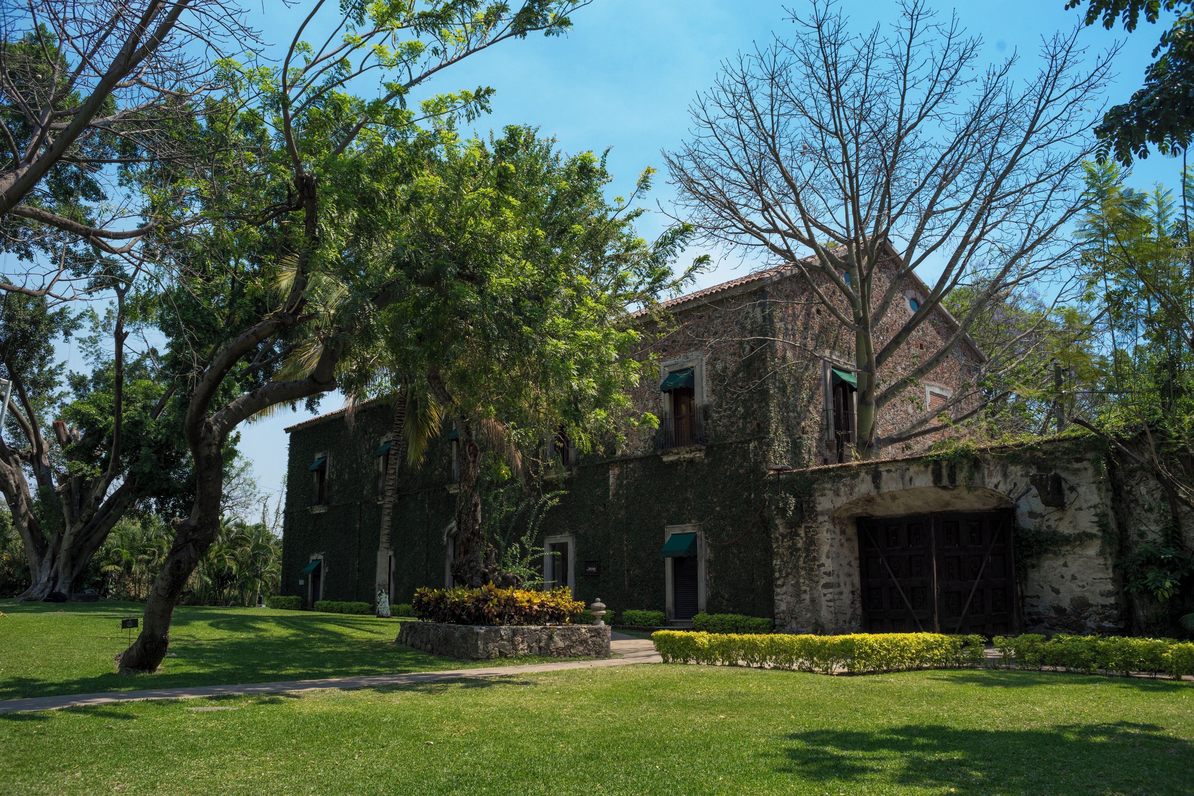 A historic building with a stone facade, large windows, and a well-maintained lawn with trees and shrubs.