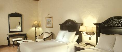 A hotel room with two beds, a desk, a chair, a lamp, and a mirror.