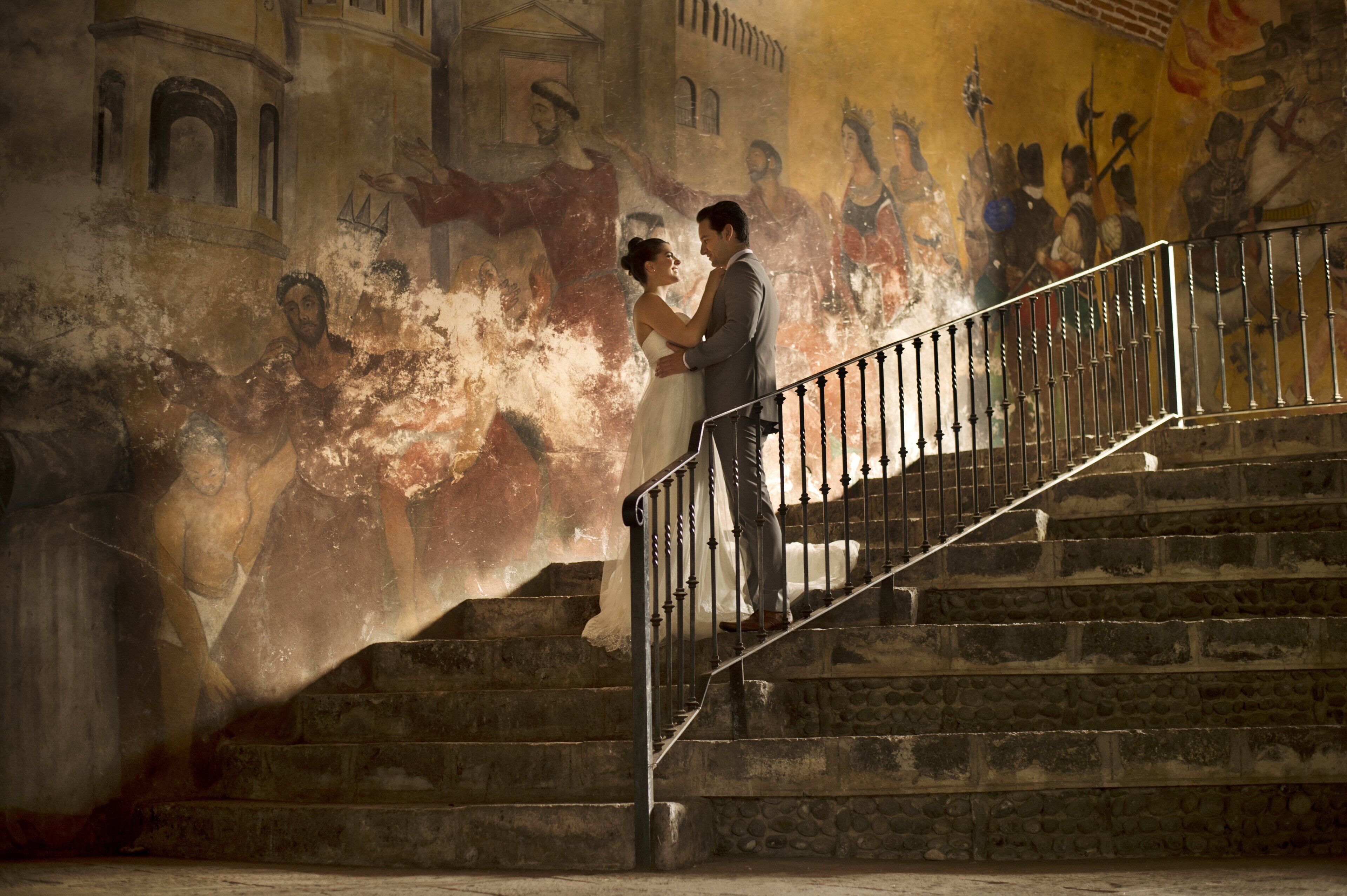 Una pareja parada en una escalera de piedra con un mural al fondo.