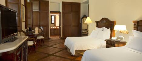A hotel room with two beds, a television, a desk with a chair, and a bathroom visible through an open door.
