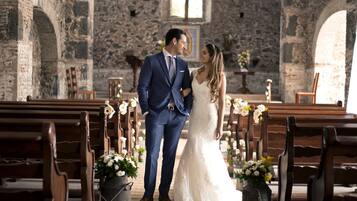 Una pareja de pie en el pasillo de una iglesia, con bancos y decoraciones florales.