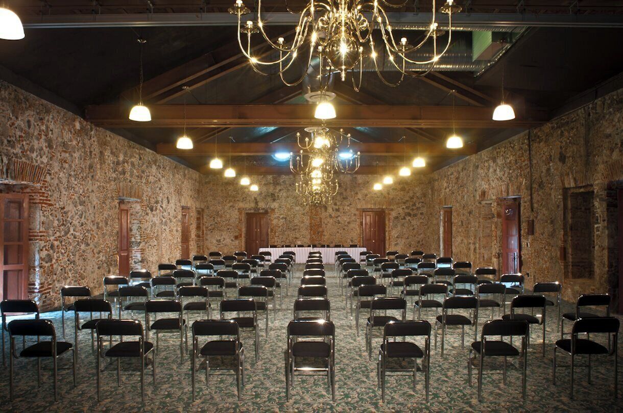 Une salle de conférence avec des rangées de chaises, un lustre, des murs en pierre et des poutres en bois.