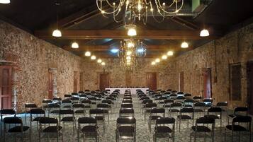 Une salle de conférence avec des rangées de chaises, un lustre, des murs en pierre et des poutres en bois.