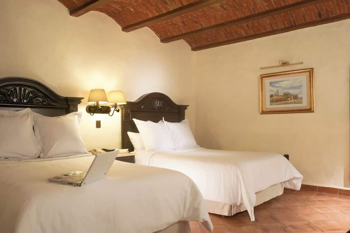Ein Hotelzimmer mit zwei Betten, einem Laptop auf einem Bett und einem Gemälde an der Wand.