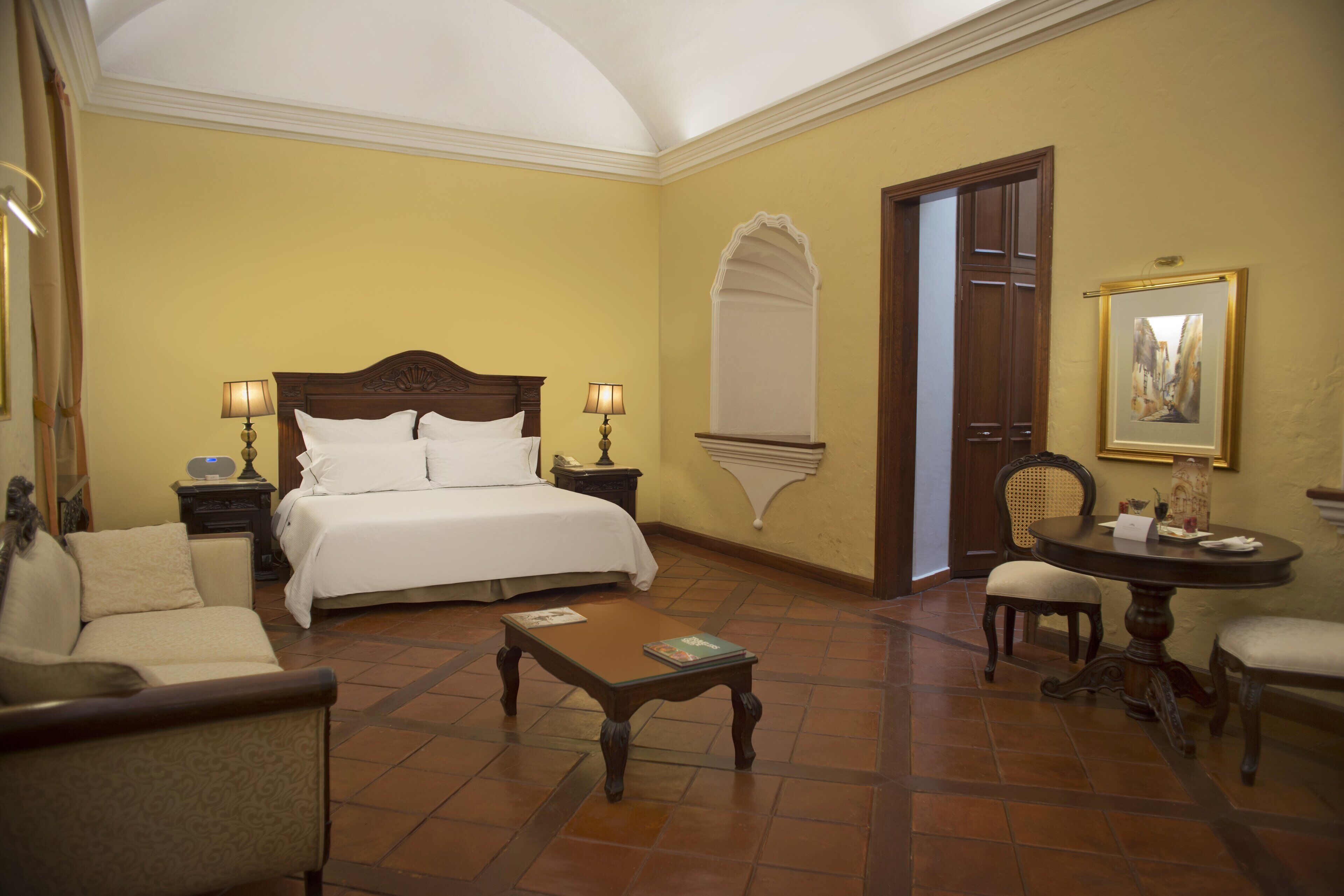 A hotel room with a bed, two bedside tables, a coffee table, a sofa, and a chair.