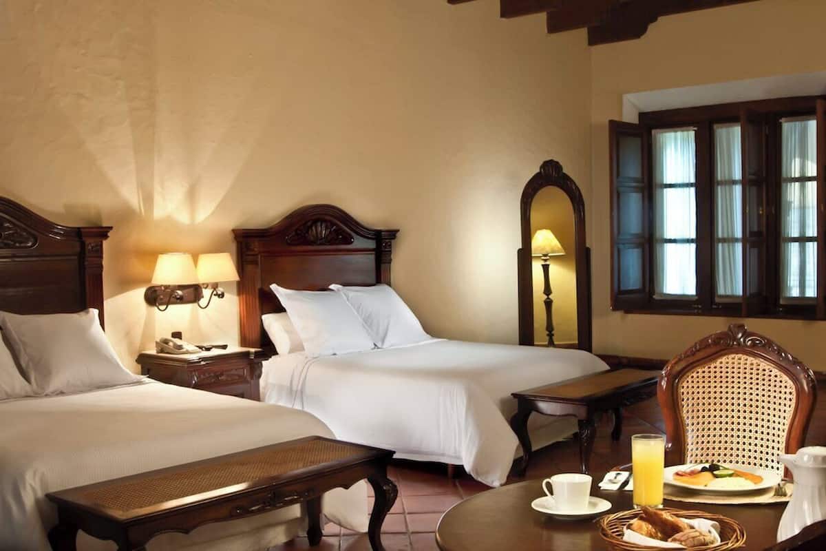 Ein Hotelzimmer mit zwei Betten, einem Frühstückstisch und einem Vorhangfenster.