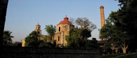 Un edificio histórico con una cúpula roja y un campanario, rodeado de árboles y un muro de piedra.