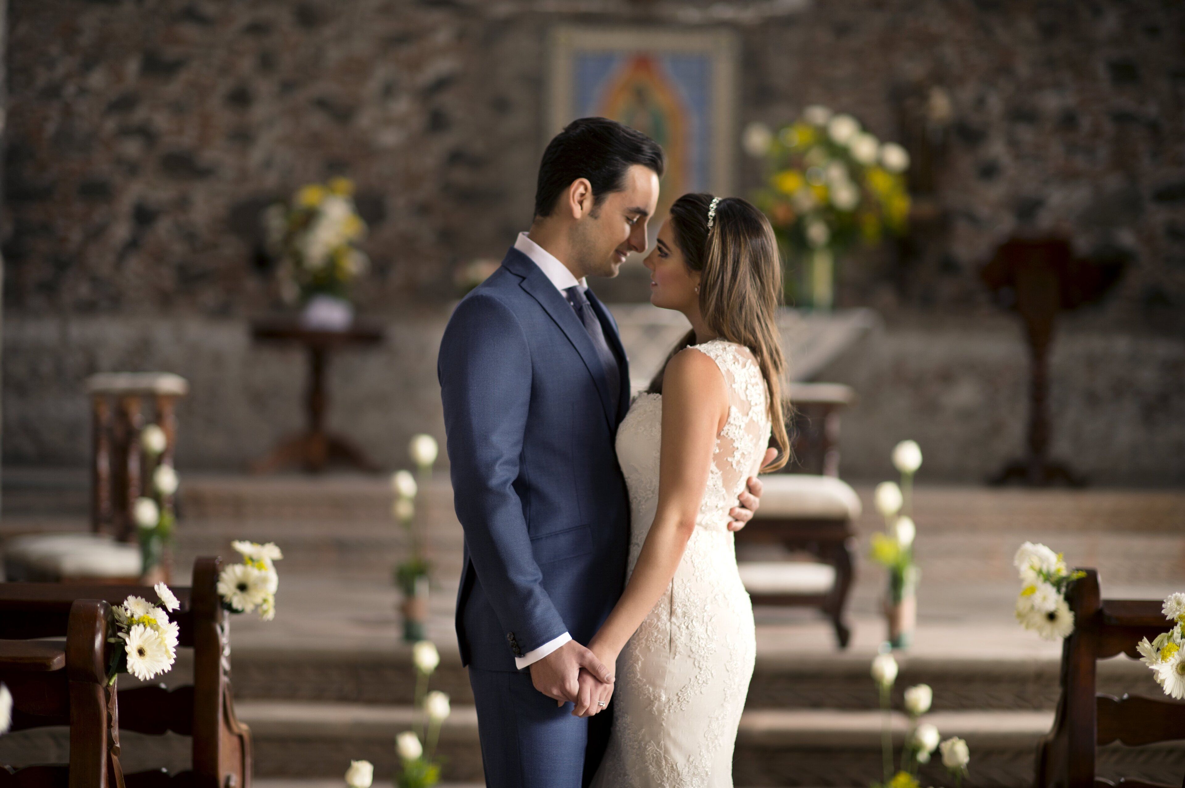 Una pareja parada en un pasillo de iglesia, con bancas y decoración floral.
