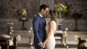 Una pareja parada en un pasillo de iglesia, con bancas y decoración floral.