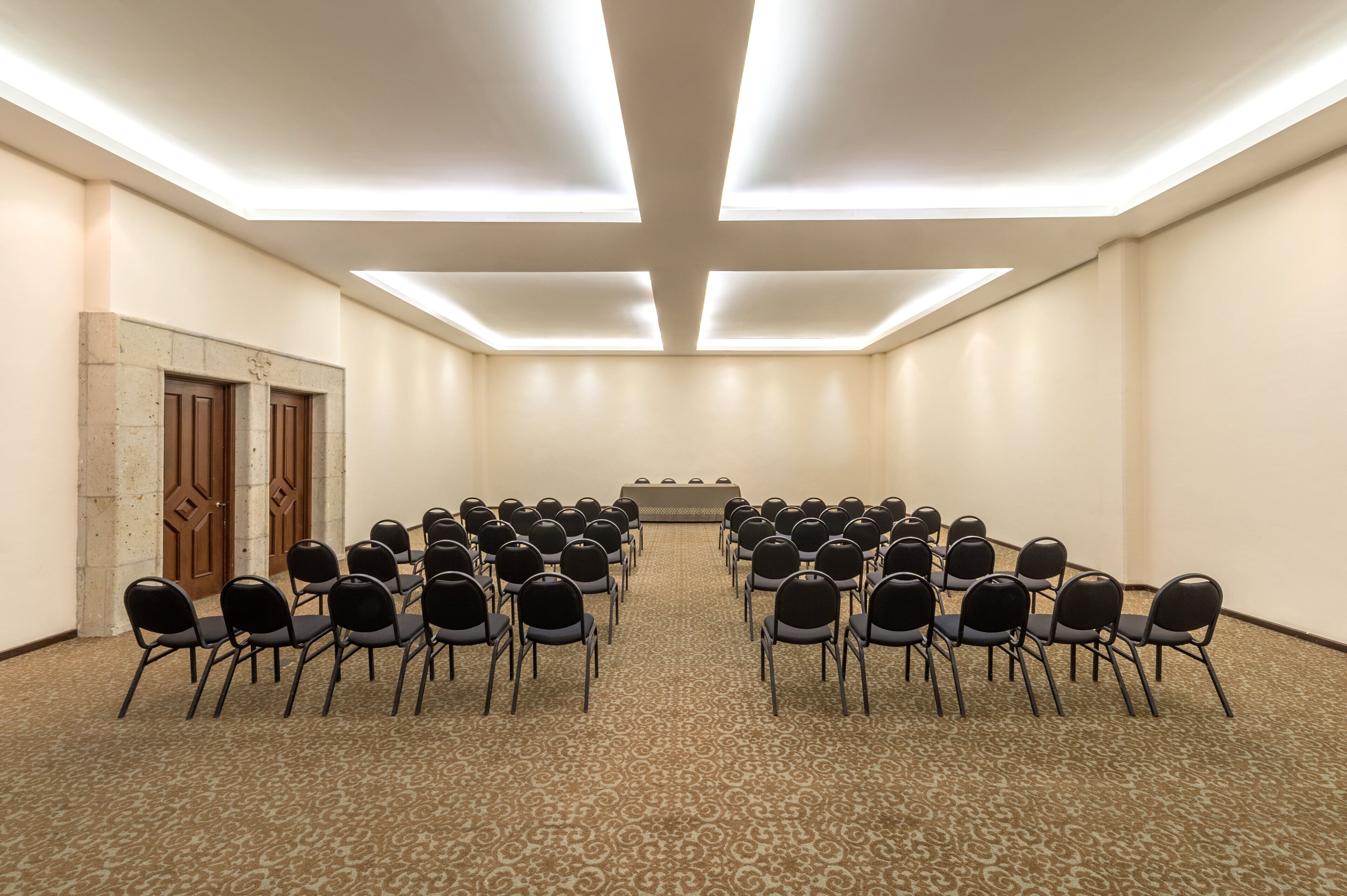 A conference room with rows of chairs facing a podium, a carpeted floor, and a high ceiling with recessed lighting.