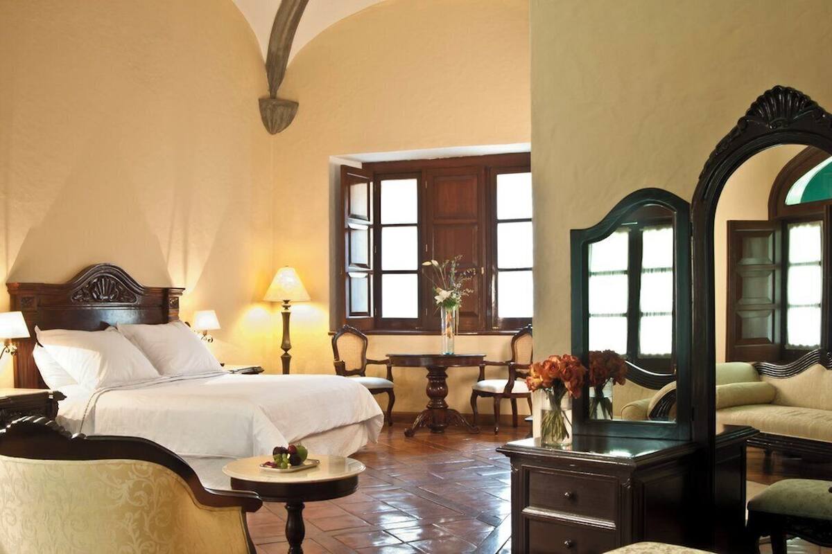 Ein Hotelzimmer mit einem großen Bett, einem Schreibtisch, einem Sessel, einem kleinen Tisch und einem Spiegel.