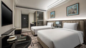 Une chambre d’hôtel avec deux lits, une télévision, un bureau avec une tasse et un livre, et une moquette à motifs.