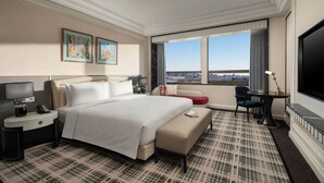 Une chambre d’hôtel avec un grand lit, un bureau avec une lampe, une télévision, un canapé et une vue sur la ville.