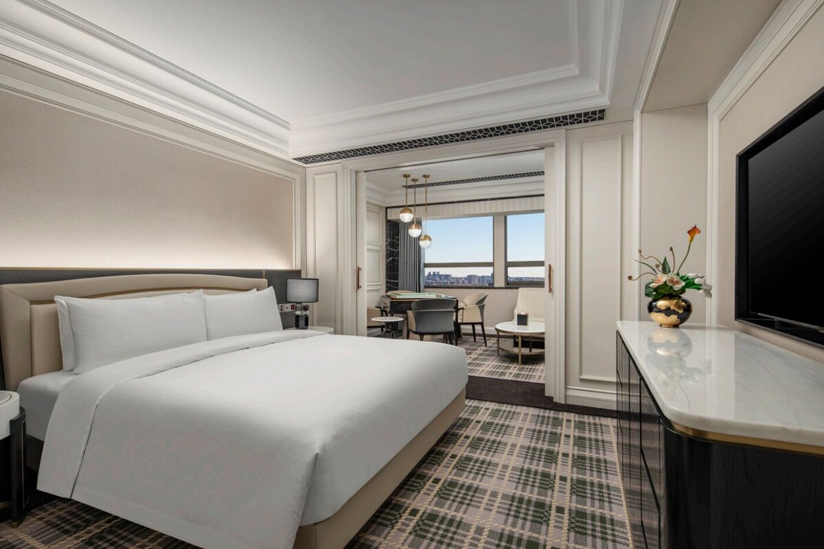 A hotel room with a large bed, a desk, a chair, a TV, and a city view.
