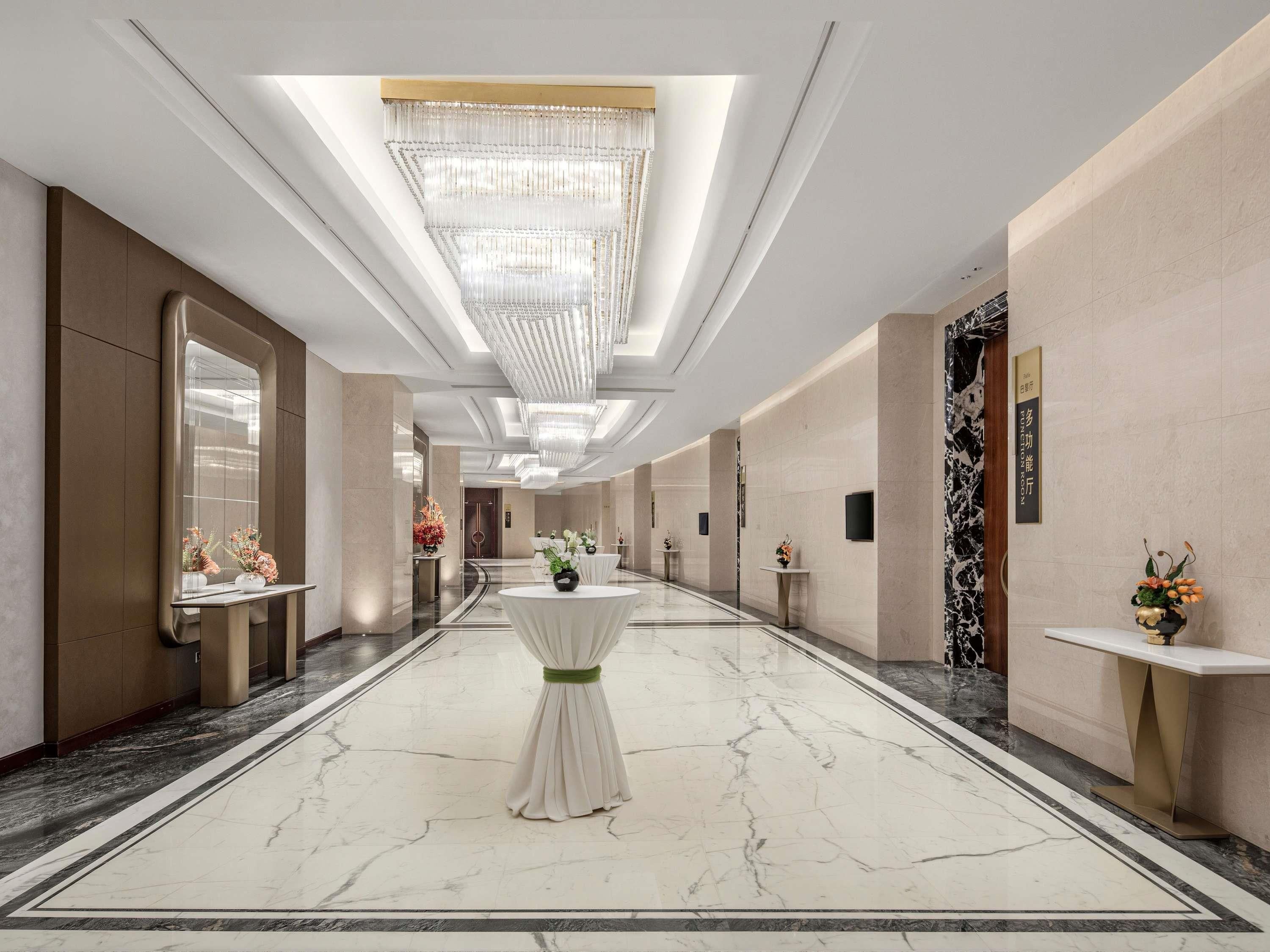 Corredor de hotel com pisos de mármore, lustres e decoração moderna.