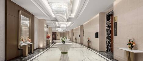 Corredor de hotel com pisos de mármore, lustres e decoração moderna.