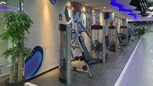 Une salle de sport moderne équipée de matériel d’exercice, ornée d’une grande fresque murale et agrémentée de plantes en pot.
