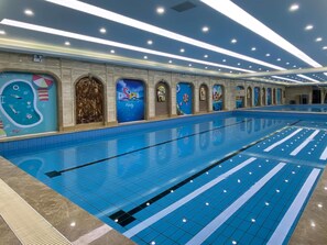 A large indoor swimming pool with multiple lanes, a tiled floor, and a ceiling with recessed lighting.
