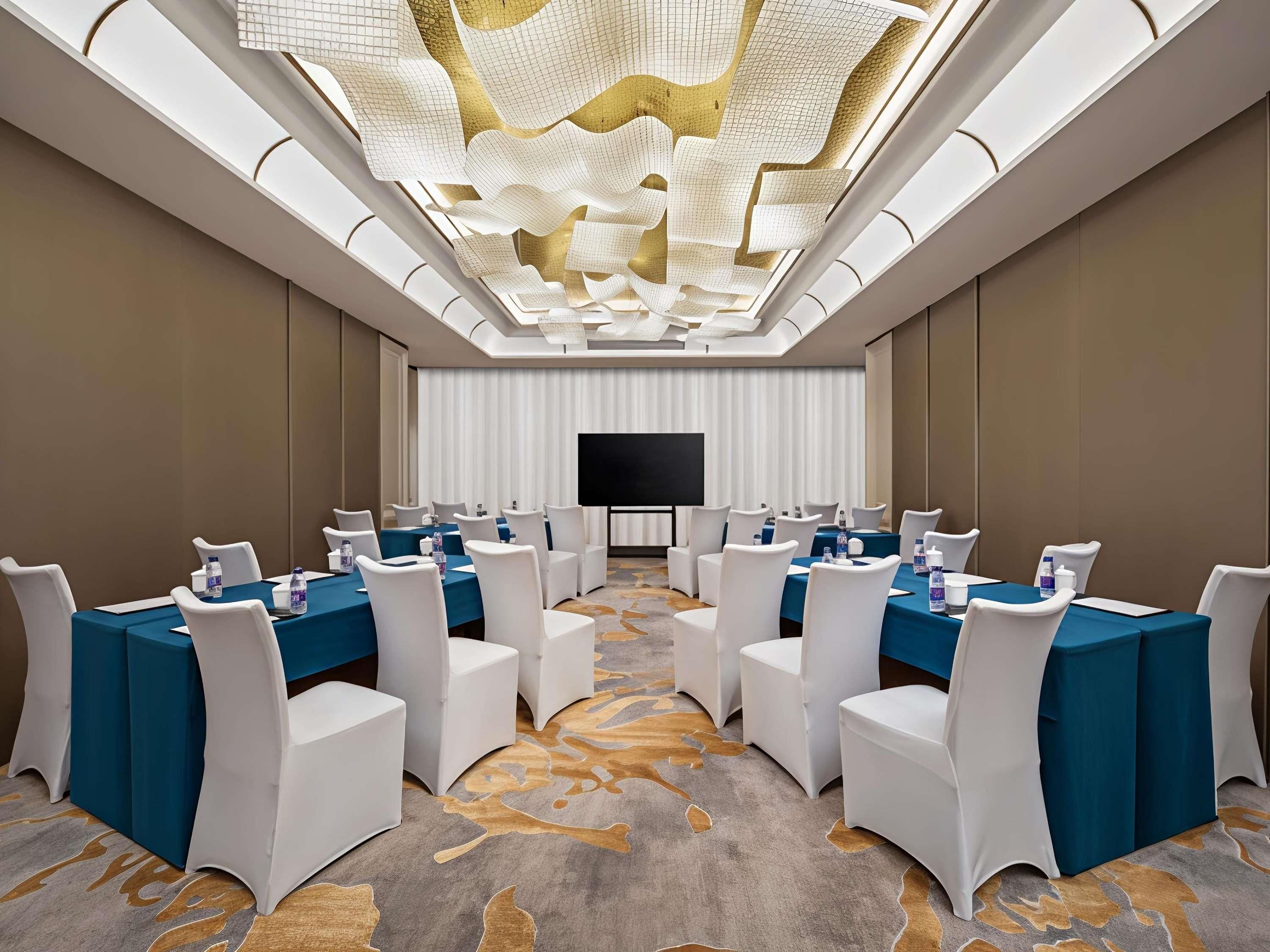 A conference room with tables, chairs, a flat-screen TV, and a patterned carpet.