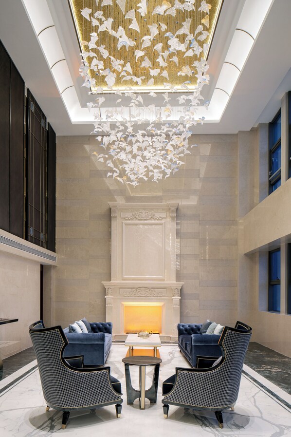 A lobby with a fireplace, two sofas, and a chandelier with hanging elements. - Pullman Beijing South - Newly Renovated (Beijing)