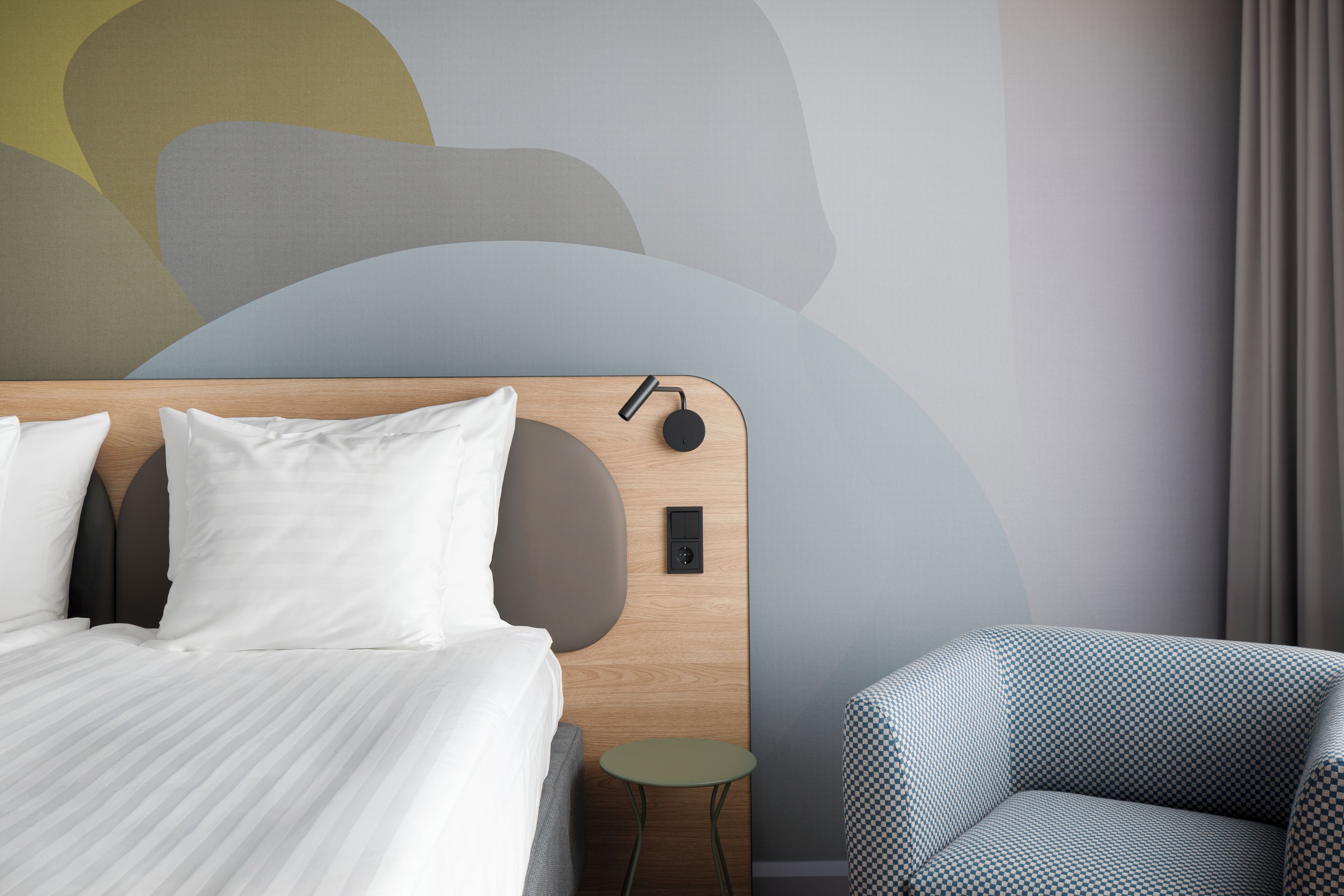 Una habitación de hotel moderna con un cabecero de madera, una mesita auxiliar pequeña y un sillón con estampado.