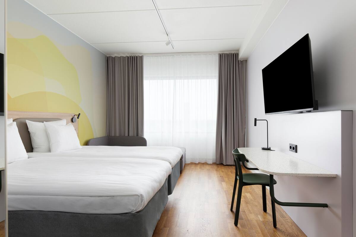 A hotel room with a bed, a desk, a chair, a TV, and a window with curtains.