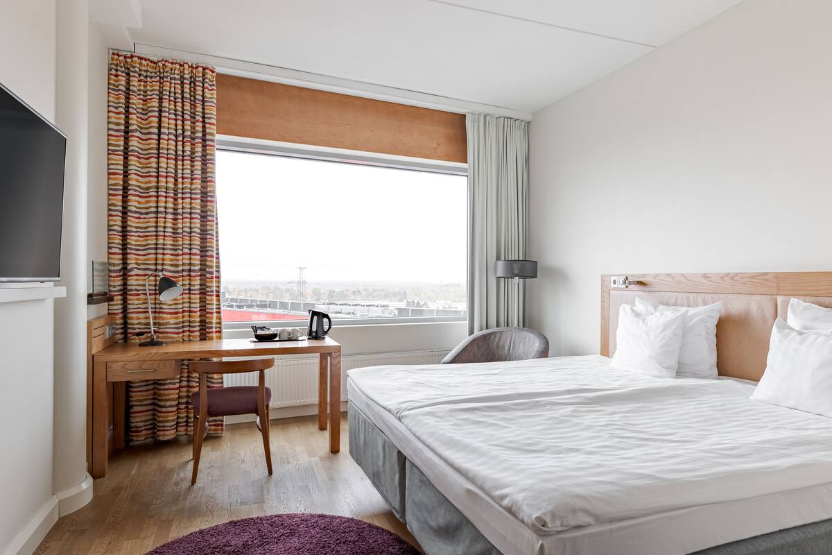 A hotel room with a bed, a desk, a chair, a TV, and a window with curtains.
