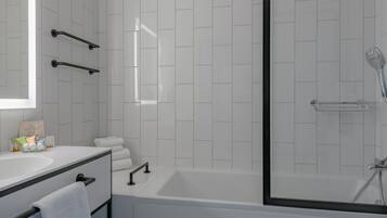 Ein modernes Badezimmer mit weiß gefliester Wand, einer Badewanne, einer Dusche und einem Waschtisch mit Spiegel und Handtuchhalter.