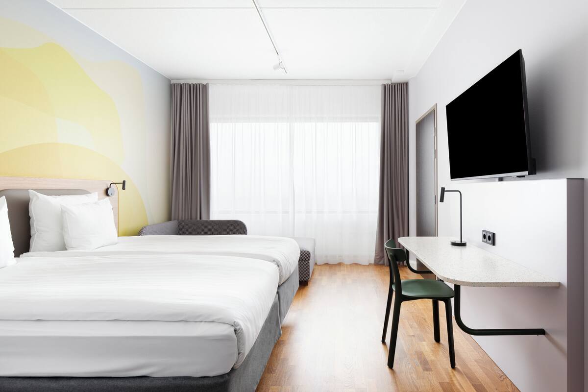 A hotel room with a bed, a desk, a chair, a TV, and a window with curtains.