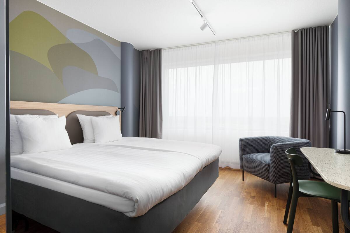 A modern hotel room with a large bed, a small table, and a chair.
