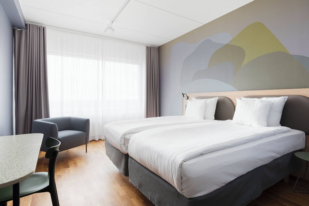 A hotel room with a large bed, a desk, and a chair.