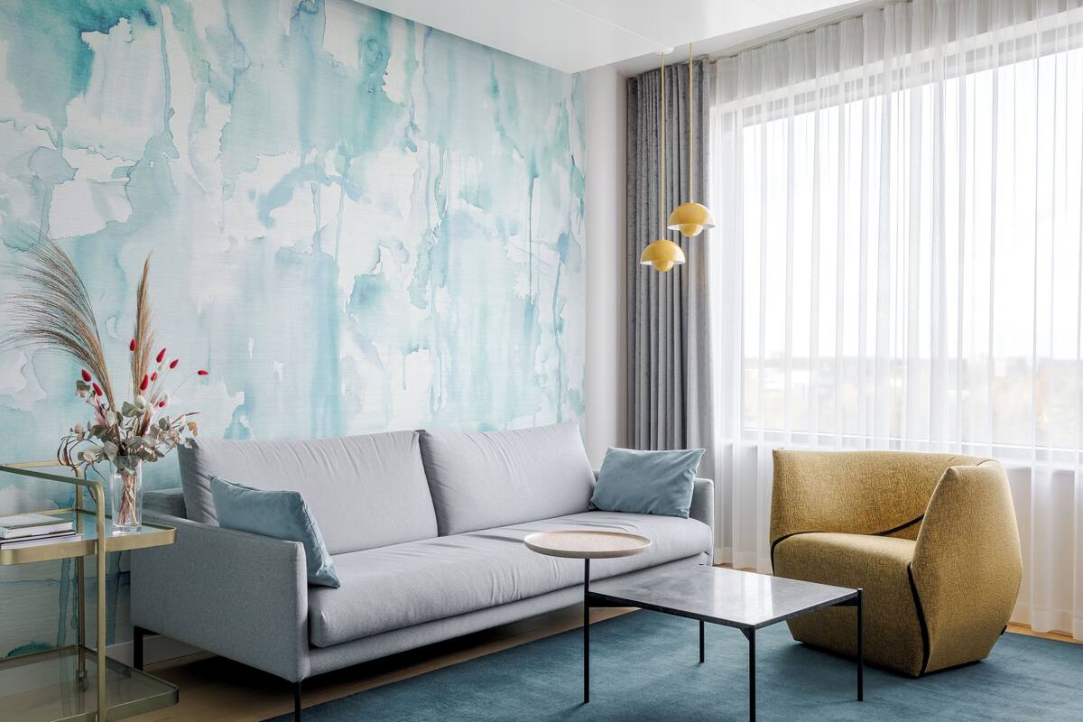 A modern living room with a grey sofa, a round coffee table, a yellow armchair, and a glass side table with a vase.