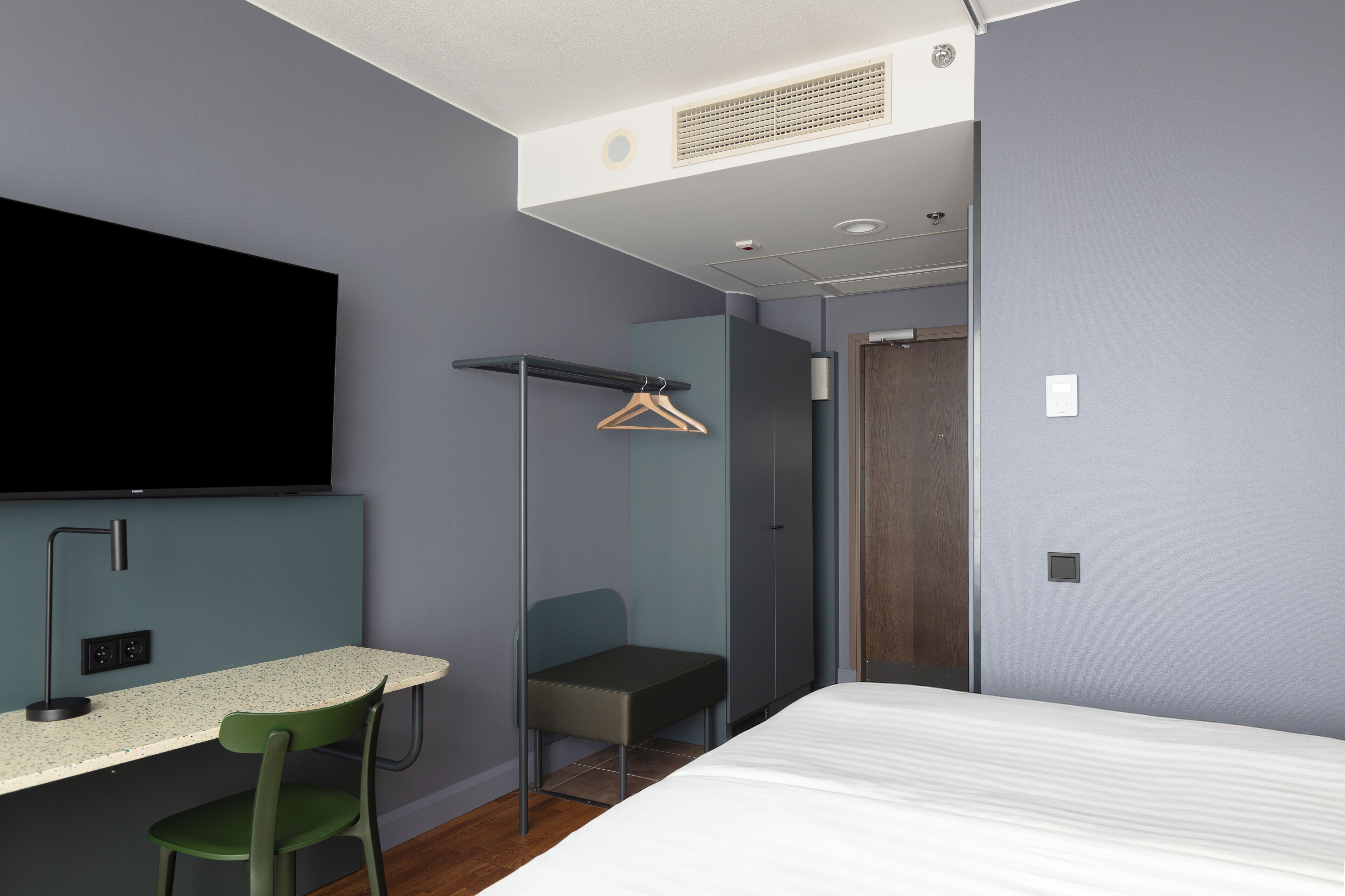 Habitación de hotel moderna con cama, escritorio, silla, televisor y armario.