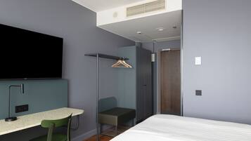 Habitación de hotel moderna con cama, escritorio, silla, televisor y armario.