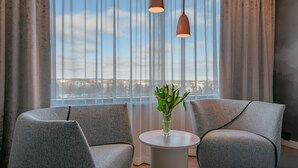 A modern room with two grey armchairs, a small round table, a vase with green plants, and a view of a cityscape through sheer curtains. - Break Sokos Hotel Flamingo (Vantaa)