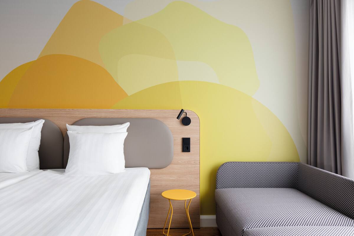 A modern hotel room with a bed, a small round table, and a sofa.