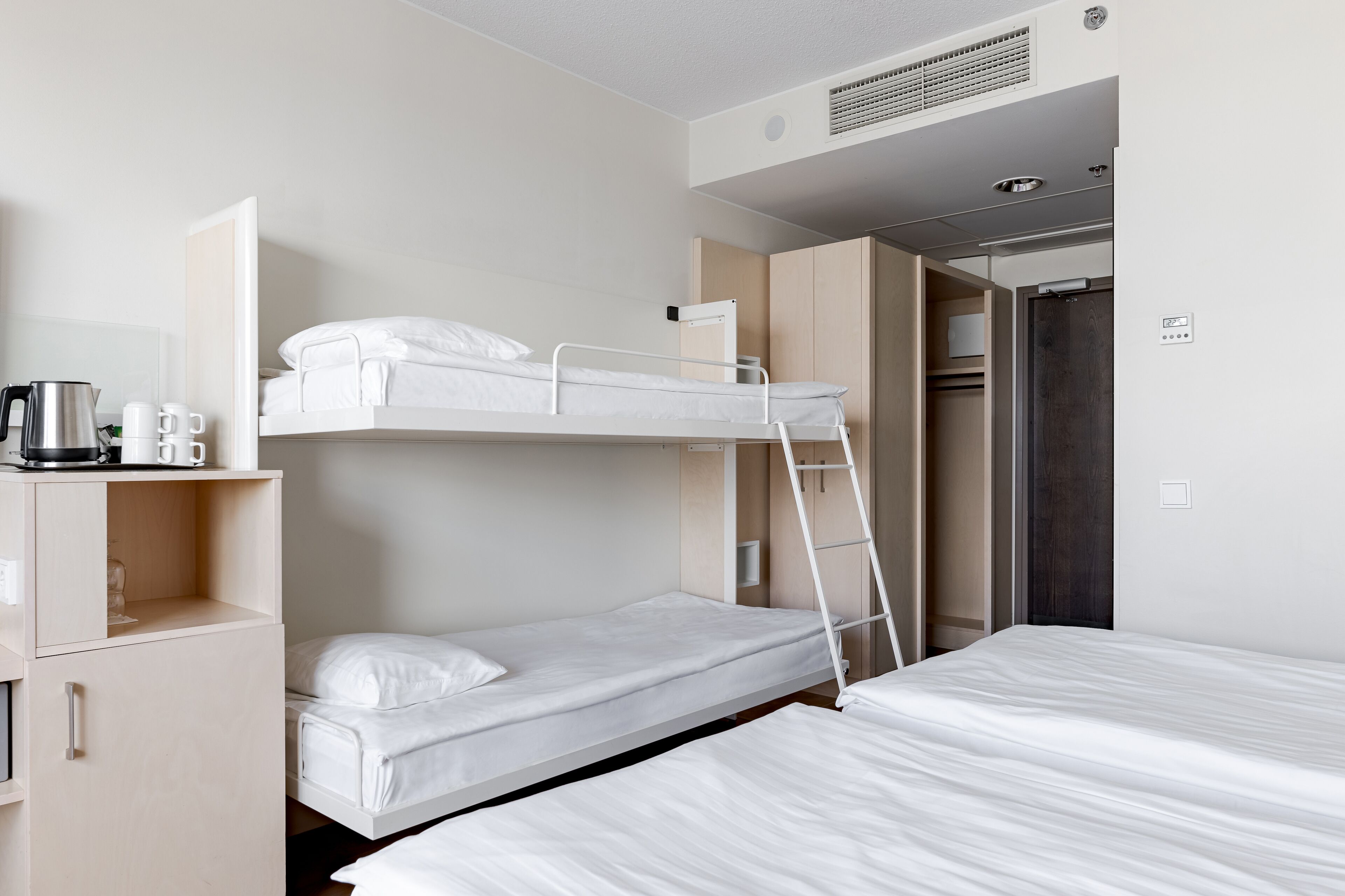 A bunk bed room with a desk, a coffee maker, and a wardrobe.