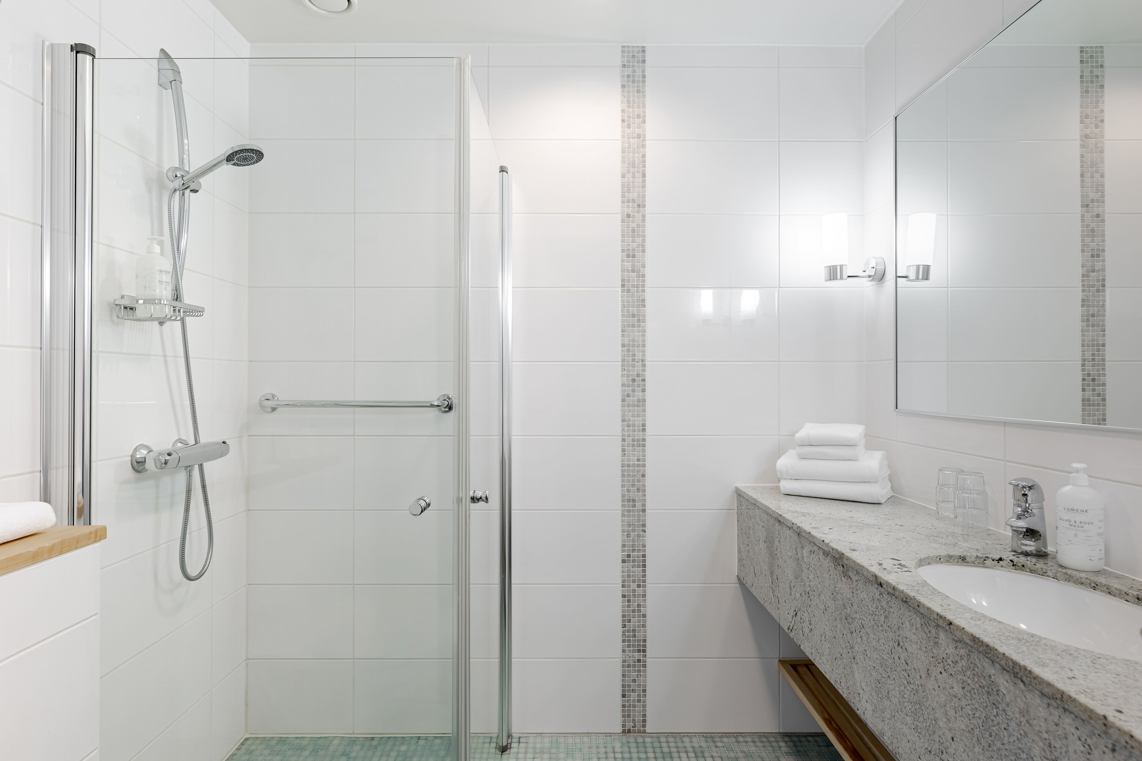 A modern bathroom with a glass shower enclosure, a tiled shower area, a sink with a marble countertop, and a mirror above the sink.
