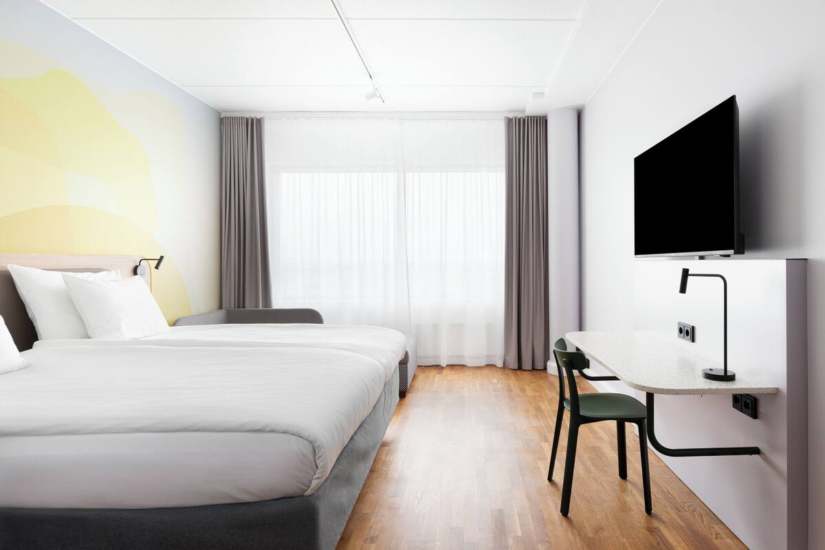 A modern hotel room with a large bed, a desk, and a flat-screen TV.